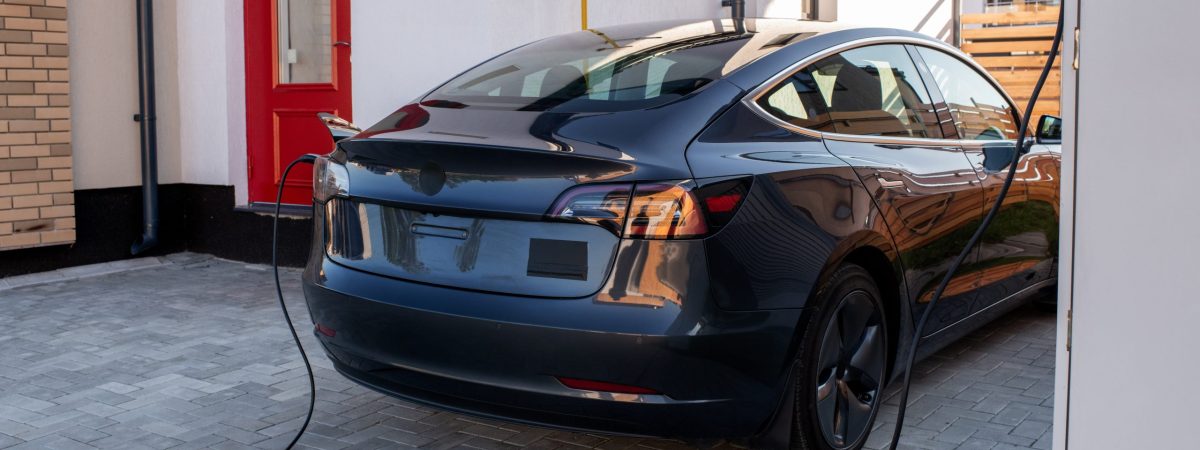 New black electric car is being charged at station in urban environment